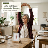 Frau ab 60 hebt am Esstisch im Sitzen die Arme über den Kopf, vor ihr steht eine Karte aus dem Starter Set