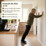 Mann ab 60 macht in der Küche einen Liegestütz an der Wand, auf der Arbeitsplatte steht die passende Karte