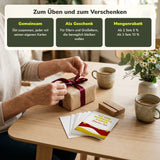 Hände packen ein Geschenk aus, daneben liegen die Karten des Starter Sets auf dem Tisch