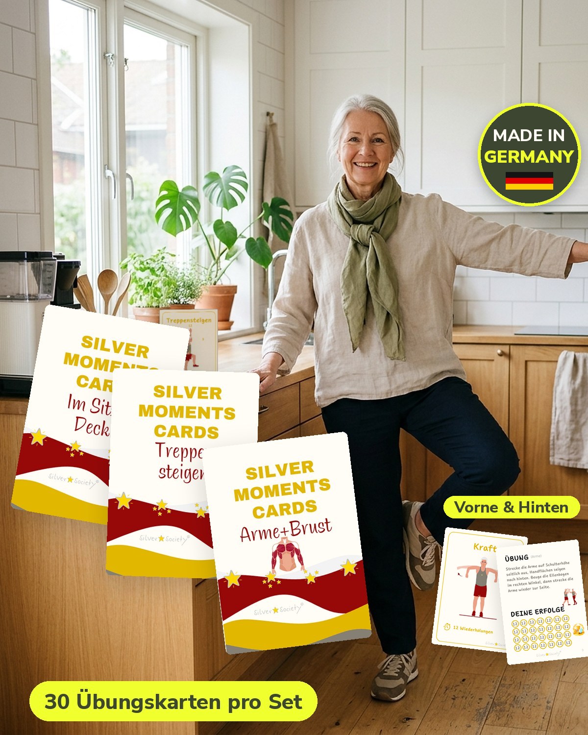 Frau ab 60 übt in der Küche auf einem Bein, im Vordergrund die Kartensets Im Sitzen, Treppensteigen und Arme + Brust der Silver Moments Cards