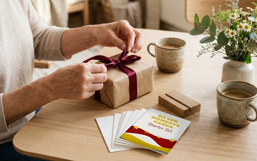 Frau ab 60 öffnet am Wohnzimmertisch ein Geschenk mit dem Silver Moments Cards Starter Set